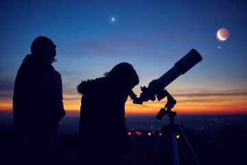 Mother and daughter observing stars, planets, Moon and night sky with astronomical telescope.