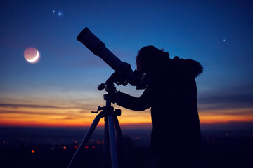 Child girl observing stars, planets, Moon and night sky with astronomical telescope.