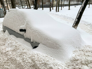 The car is completely covered with snow after a heavy snowfall.