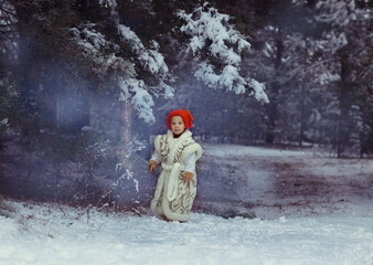 Fototapeta na wymiar the snow maiden girl in a red cap, a white beautiful vest with patterns stands near a glowing garland that weighs on a pine branch in a snowy forest