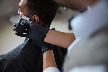 Handsome male in black peignoir resting while getting hairdressing in barber shop