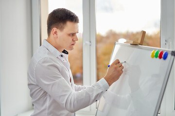 Young man in a white shirt in the office by the window with a flipchart.
