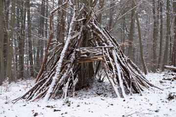 Schneebedeckte Hütte aus Ästen an einem Baum im Wald