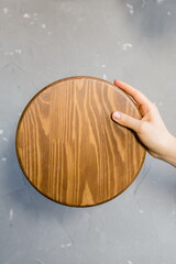 A wooden cutting board is held by a female hand on a gray background. Place for text.