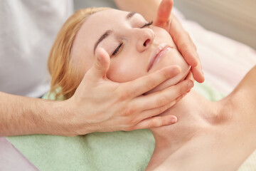 Fototapeta premium Facial massage. A woman is given a massage in a beauty salon. Close-up.