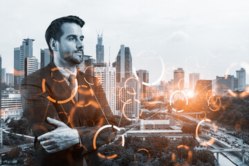 A young Caucasian businessman in crossed arms pose pondering on technology at business process to achieve tremendous growth. Tech hologram icons over Kuala Lumpur background