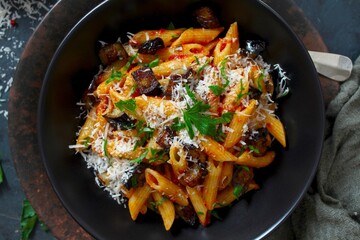 Pasta alla norma - Italian pasta with eggplant, tomato and parmesan cheese on dark table. Top view with copy space.