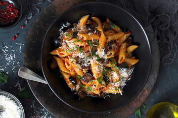 Pasta alla norma - Italian pasta with eggplant, tomato and parmesan cheese on dark table. Top view...