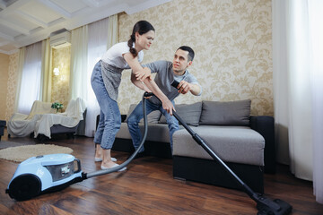 Wife vacuums the room and prevents her husband from watching TV