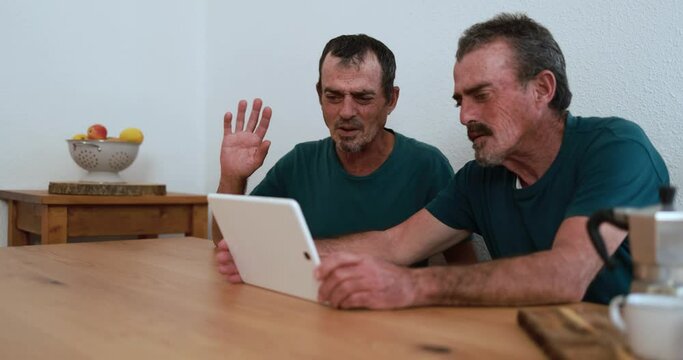 Twin brother senior men having fun on a video call with digital tablet at home 