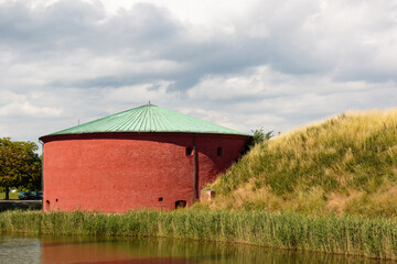 round red granary next to a pond and an earth mound