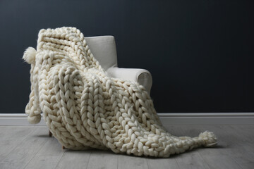 Fototapeta na wymiar Soft knitted blanket on armchair in living room. Interior element