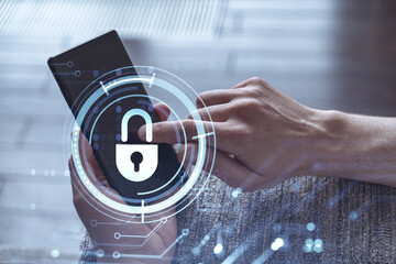 A programmer is browsing the Internet in smart phone to protect a cyber security from hacker attacks and save clients confidential data. Padlock Hologram icons over the typing hands.