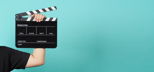 Hand is holding Black clapperboard or movie slate on green or Tiffany Blue  background.man wear...