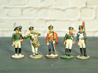 A few miniature tin soldiers stand on a gray surface against a brick wall.