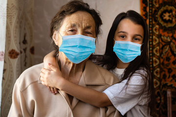 Grandmother with grandchild in a masks plays near the window of his house. Stay at home. Quarantin....