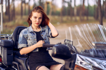 Fototapeta na wymiar Biker girlfriend in a denim jacket sits on a motorcycle.