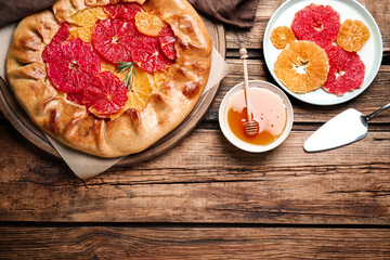 Tasty galette with citrus fruits and rosemary served on wooden table, flat lay. Space for text