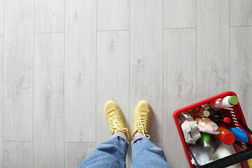 Woman and shopping basket with groceries on white wooden floor, top view. Space for text