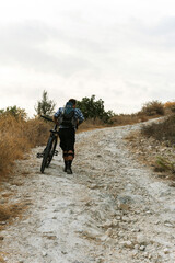 Professional downhill bicycle rider walking by mountain trail