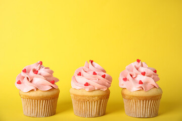Tasty cupcakes with heart shaped sprinkles on yellow background. Valentine's Day celebration