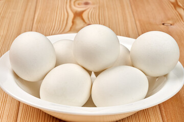 White clean chicken eggs in a plate on a wooden table. Close-up. Selective focus