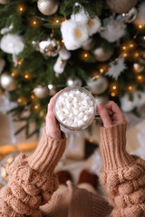 Woman with cup of delicious hot drink near Christmas tree at home, top view