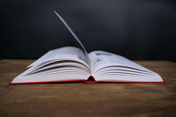 open paper book with red cover lies on a wooden table closeup, hand flipping pages, reading concept, copy space