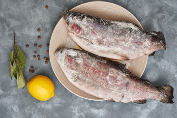 Fresh frozen river trout on a plate with lemon and pepper.Close-up