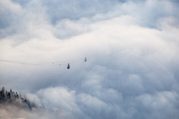 Two cable cars appearing out of the fog over the trees and out of the valley to the top of the mountatin, right after sunset in the Dolomites in Italy