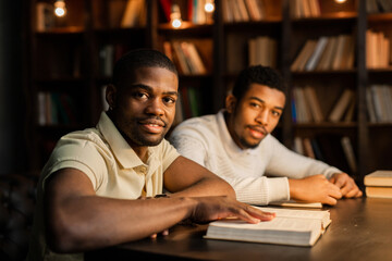 two young african men are sitting at a table with books 