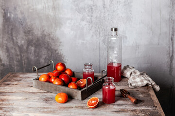 fresh blood orange juice in glasses and in bottle with fresh oranges in wooden tray on wooden table, copy space