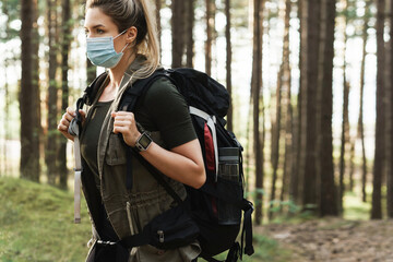 Woman hiker with a backpack wearing prevention mask during her hike in forest