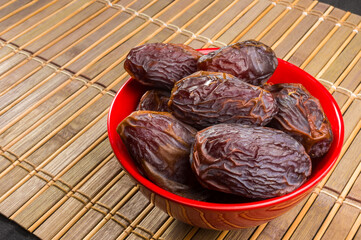 Big luxury dried date fruit in bowls on the bamboo mat, kurma ramadan kareem concept, close up.