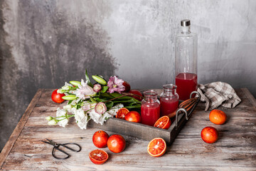 fresh blood orange juice in glasses and in bottle with fresh oranges in wooden tray on wooden table, copy space