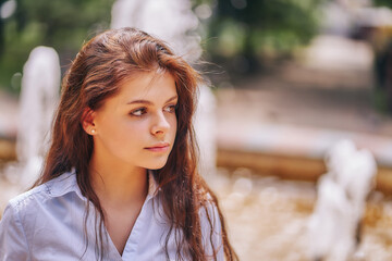 Portrait of a teenage girl in a shirt standing by a fountain in the park.