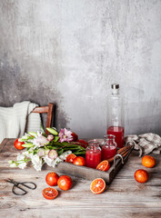 fresh blood orange juice in glasses and in bottle with fresh oranges in wooden tray on wooden table, copy space