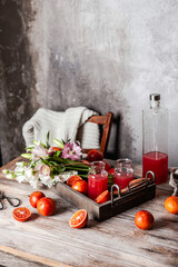 Fototapeta na wymiar fresh blood orange juice in glasses and in bottle with fresh oranges in wooden tray on wooden table, copy space