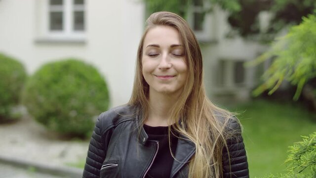 Face of young woman in the garden who is gently smiling while having her eyes closed. She's thinkingh about something nice.
