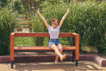Joyful, funny teenage girl fooling around on a bench in a city park.