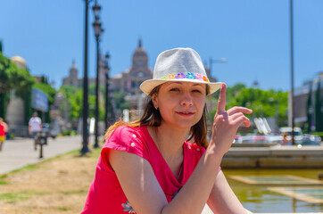 Young woman traveler with red dress and hat posing in Barcelona city in sunny summer day with blue sky, Palau Nacional or National Palace of Montjuic and National Art Museum of Catalonia background