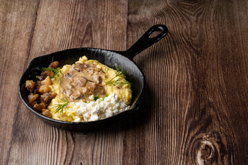 Banosh - a traditional dish in the Western Ukraine made of cornmeal. Served in a black pan with cracklings, mushrooms and hutsul cheese bryndza. Close-up on a wooden background with copy space.