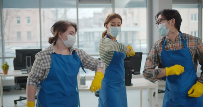 Professional office cleaning janitors in safety mask bumping elbows at workplace