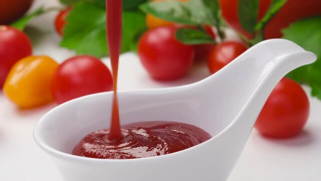 Pouring ketchup in bowl on white background, served with fresh tomatoes