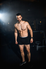 Fototapeta na wymiar Muscular athlete posing in a dark gym, portrait of a sporty man