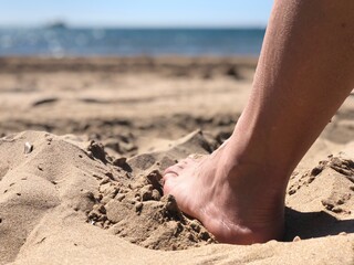 Plano detalle de un pie enterrado en la arena de la playa