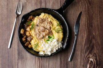 Banosh - a traditional dish in the Western Ukraine made of cornmeal. Served in a black pan with cracklings, mushrooms and hutsul cheese bryndza. Close-up top view isolated on a wooden background.