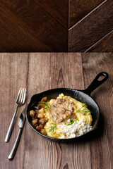 Banosh - a traditional dish in the Western Ukraine made of cornmeal. Served in a black pan with cracklings, mushrooms and hutsul cheese bryndza. Close-up on a wooden background with copy space.