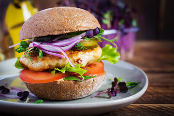 Hamburger. Sandwich with chicken burger, tomatoes,  pickled cucumber and red onion. Fresh tasty chicken burger on wooden table.