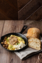 Banosh - ukrainian dish made of cornmeal. Served in black pan with cracklings, mushrooms and hutsul cheese. Close-up isolated on wooden background with sliced bread and grey linen napkin. Copy space.